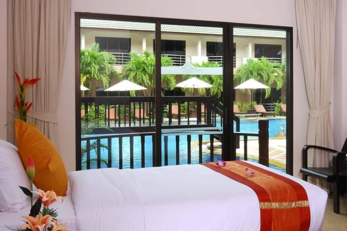 Une chambre d’hôtel avec un lit, une vue sur une piscine et des palmiers, et un balcon doté d’une balustrade.