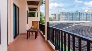 A balcony with a wooden table and chair, a small table with a vase, and a view of a construction site. - Nipa Resort (Phuket)