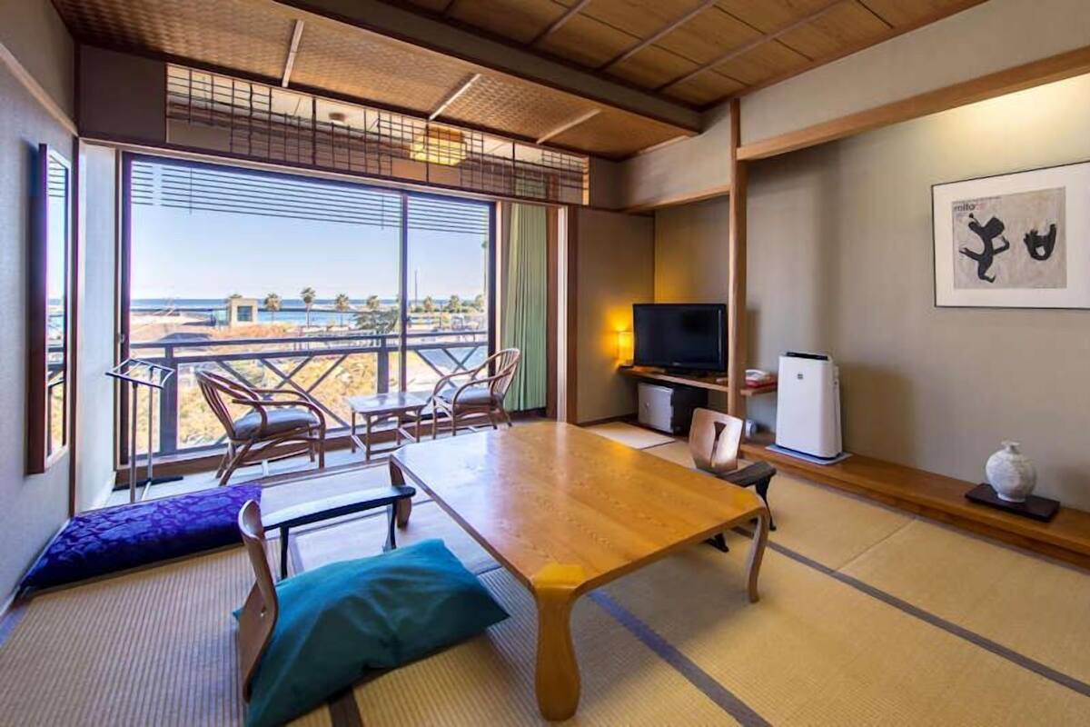 A room with tatami flooring, a low table, chairs, a television, a small refrigerator, and a framed picture on the wall.