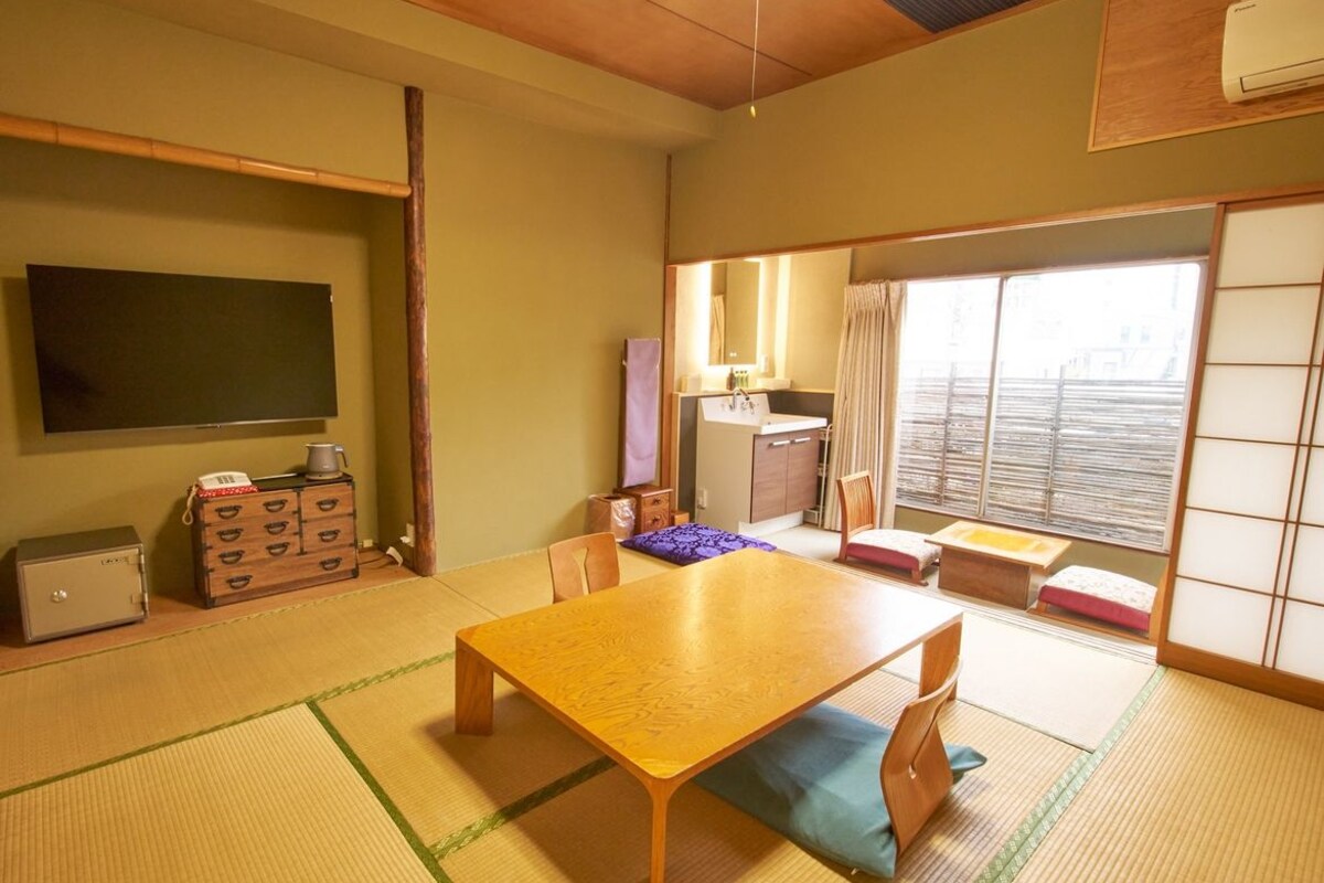 A traditional Japanese room with tatami flooring, a low wooden table, and a sliding door leading to a balcony.