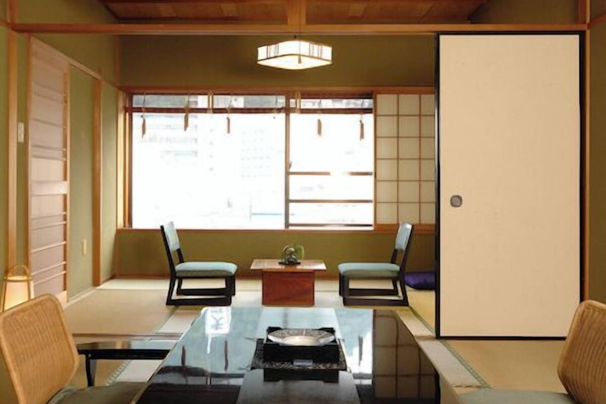 A traditional Japanese room with tatami flooring, a low table, two chairs, a sliding door, and a shoji screen.