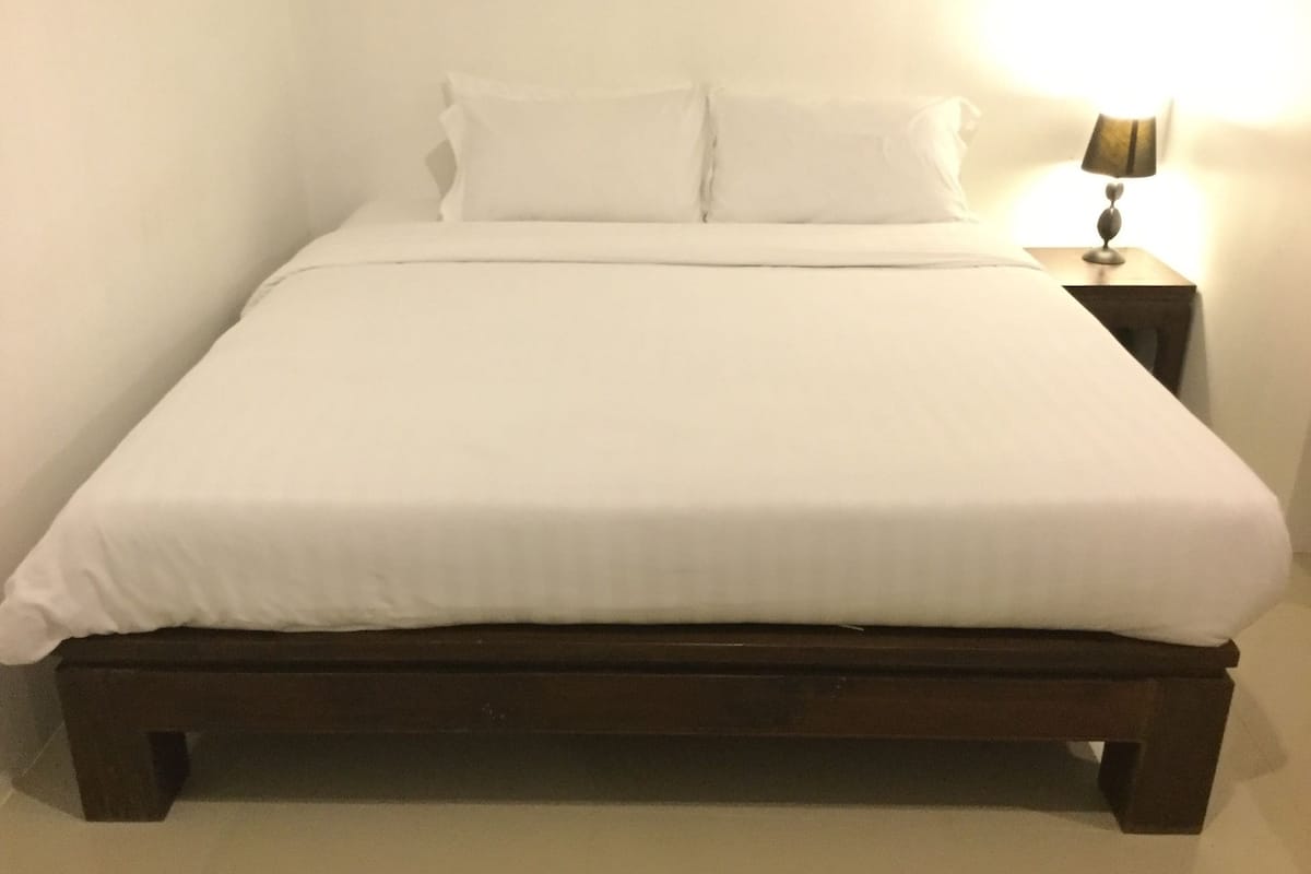 A single bed with white bedding, a wooden headboard, and a nightstand with a lamp.