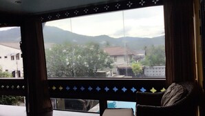 Une pièce dotée d’une grande fenêtre, d’un canapé et offrant une vue sur un quartier résidentiel avec des maisons et des montagnes.