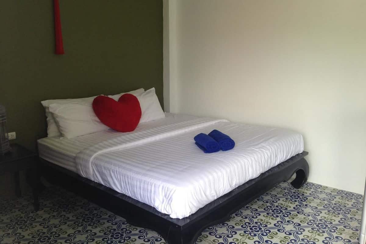 A neatly made bed with white bedding, a red heart pillow, and two rolled blue towels.
