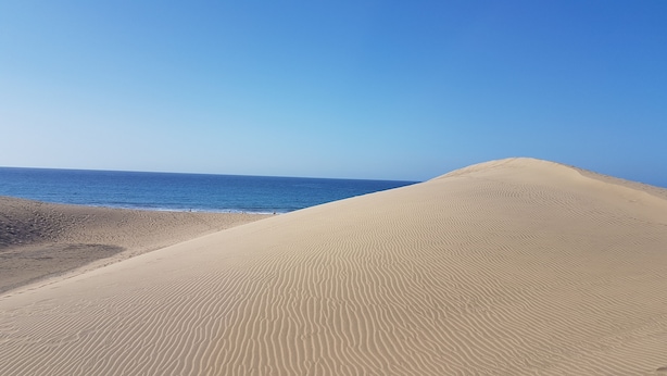 Ein sandiger Strand mit blauem Himmel und ruhiger See.