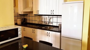 Eine kleine Küche mit weißen Schränken, einer schwarzen Arbeitsplatte, einem weißen Kühlschrank und einer Mikrowelle.