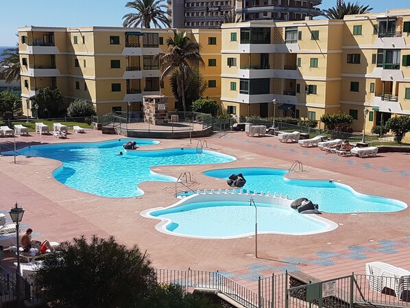A hotel with multiple swimming pools, a palm tree, and a view of the ocean.