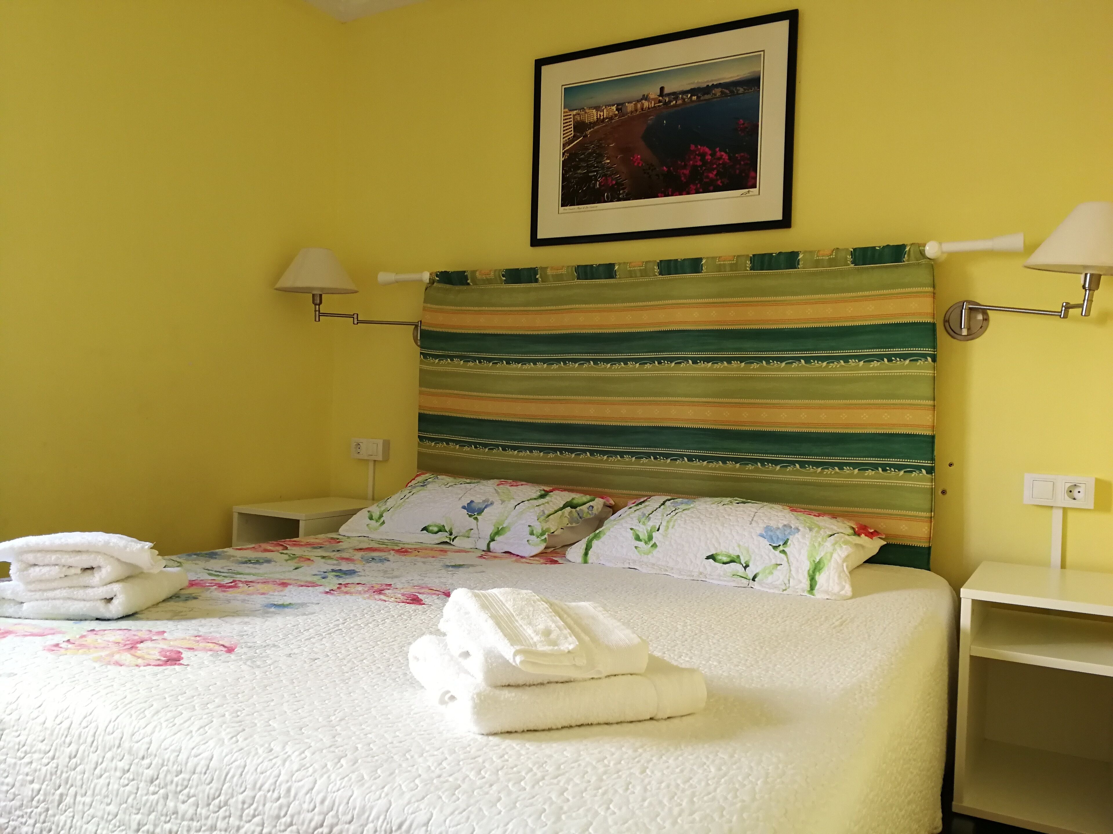 Ein Hotelzimmer mit einem gestreiften Kopfteil, floralem Bettzeug und einem gerahmten Bild an der Wand.