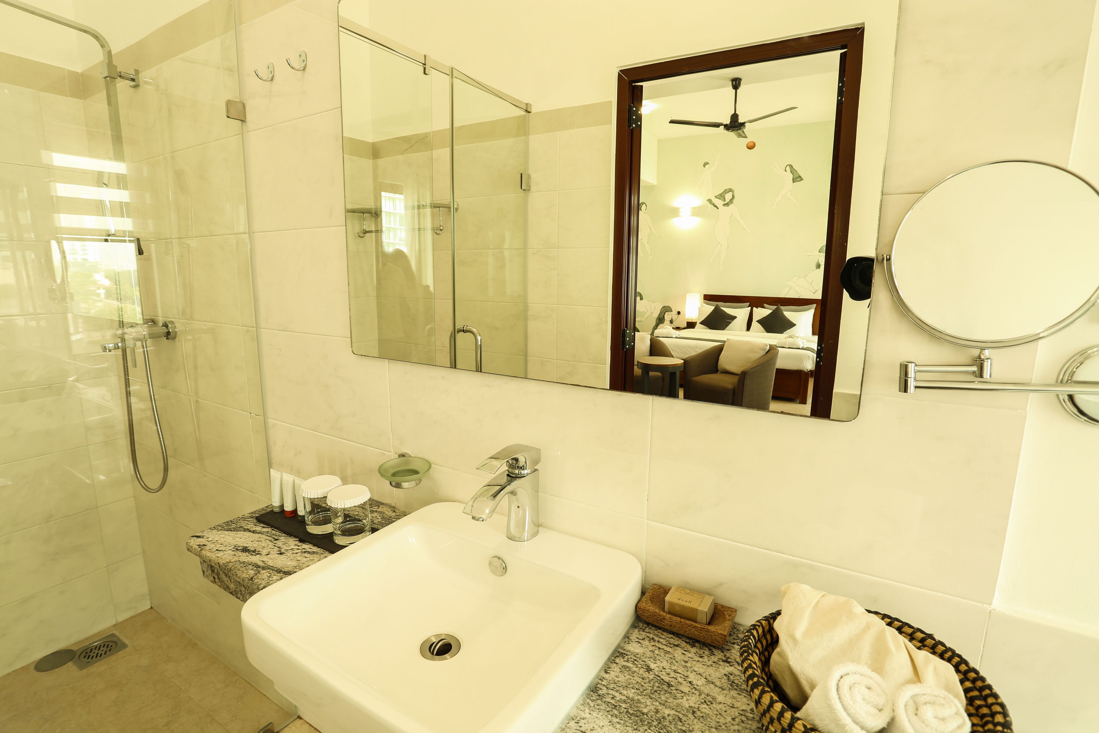 Un baño moderno con ducha de vidrio, un lavabo con encimera de mármol y un espejo con ventilador de techo.