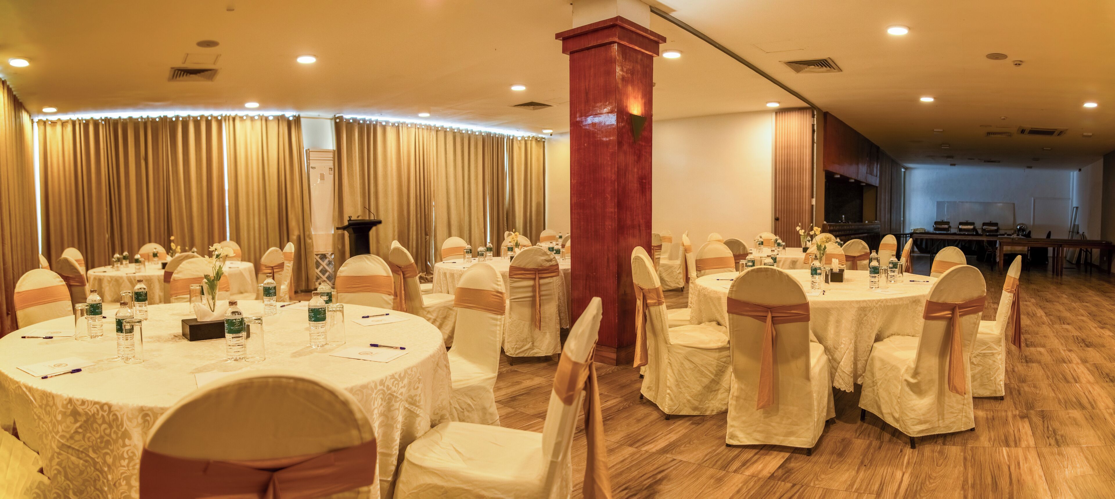 A banquet hall with round tables, white tablecloths, and chairs with beige sashes.