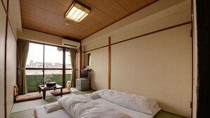 A hotel room with a bed, a small table with a chair, a television, and a view of the city through a large window. - Hotel Omiya (Kyoto)