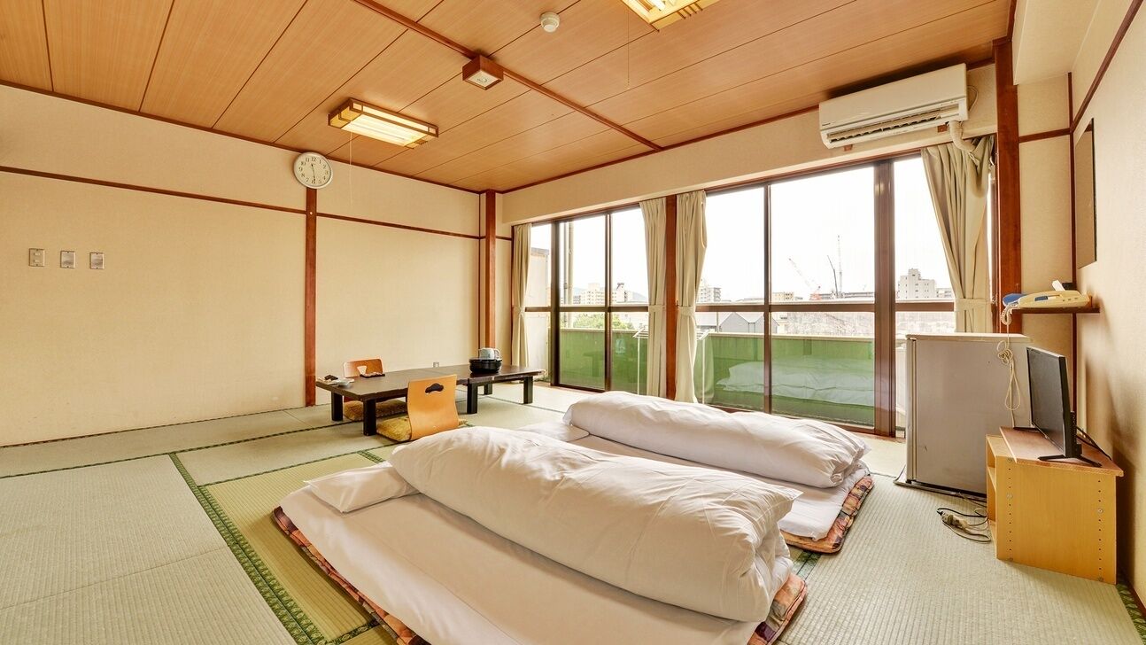 A room with tatami mats, a bed, a desk, a chair, a television, and a window with a view.