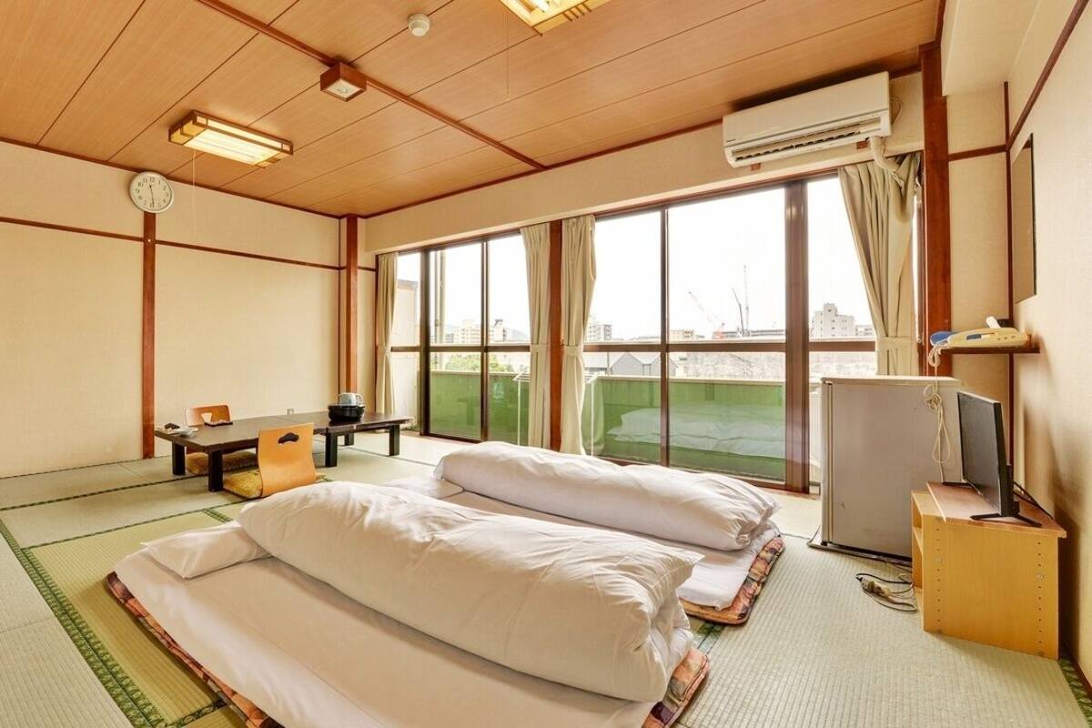 Habitación con esteras de tatami, una cama, un escritorio, una silla, un televisor y una ventana con vistas.