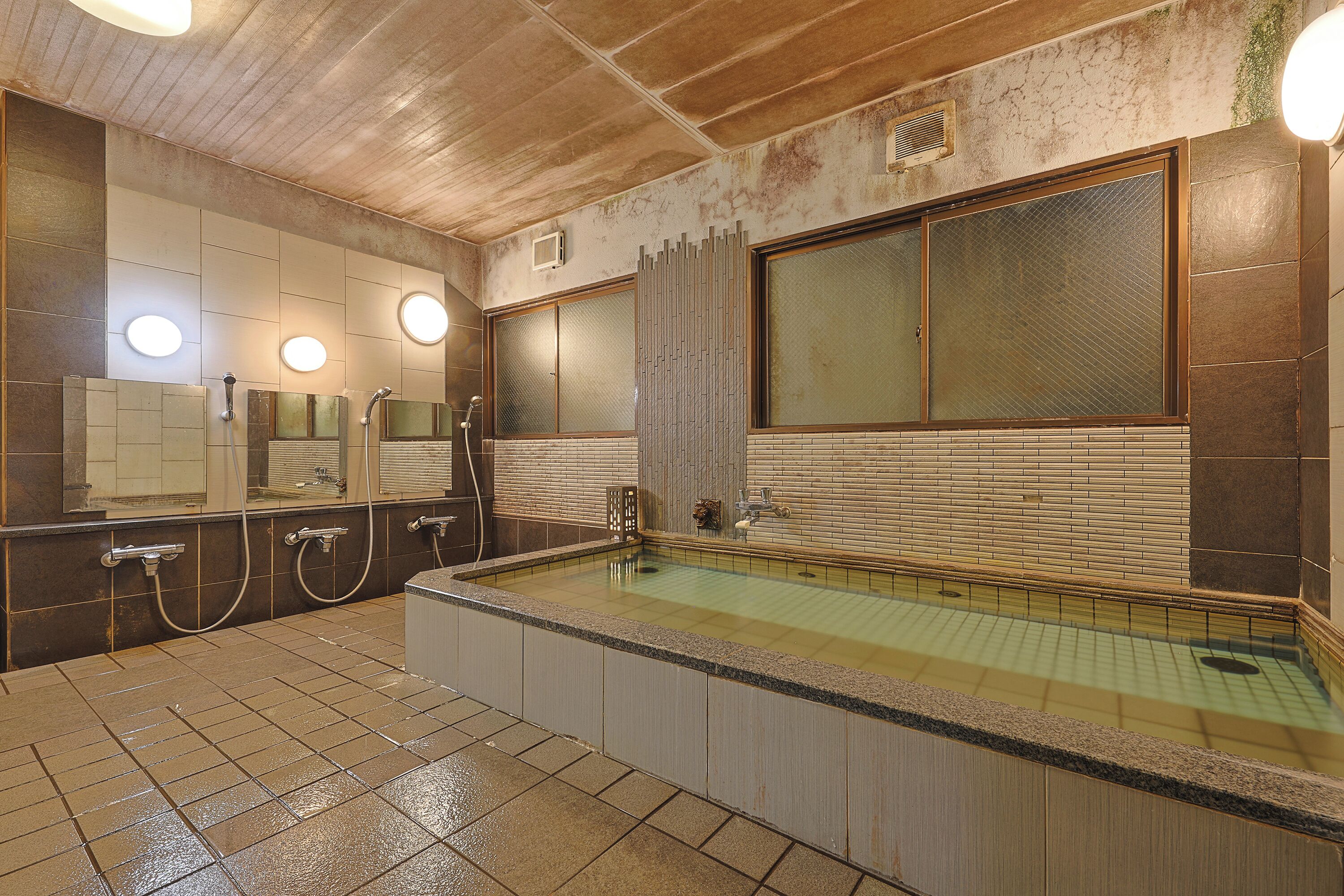 A public bath area with a large window, multiple mirrors, and a tiled floor.