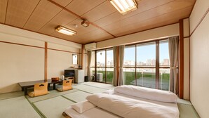 A hotel room with tatami flooring, a bed, a desk with a chair, a television, and a large window with a city view. - Hotel Omiya (Kyoto)