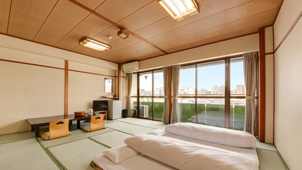 A hotel room with tatami flooring, a bed, a desk with a chair, a television, and a large window with a city view. - Hotel Omiya (Kyoto)