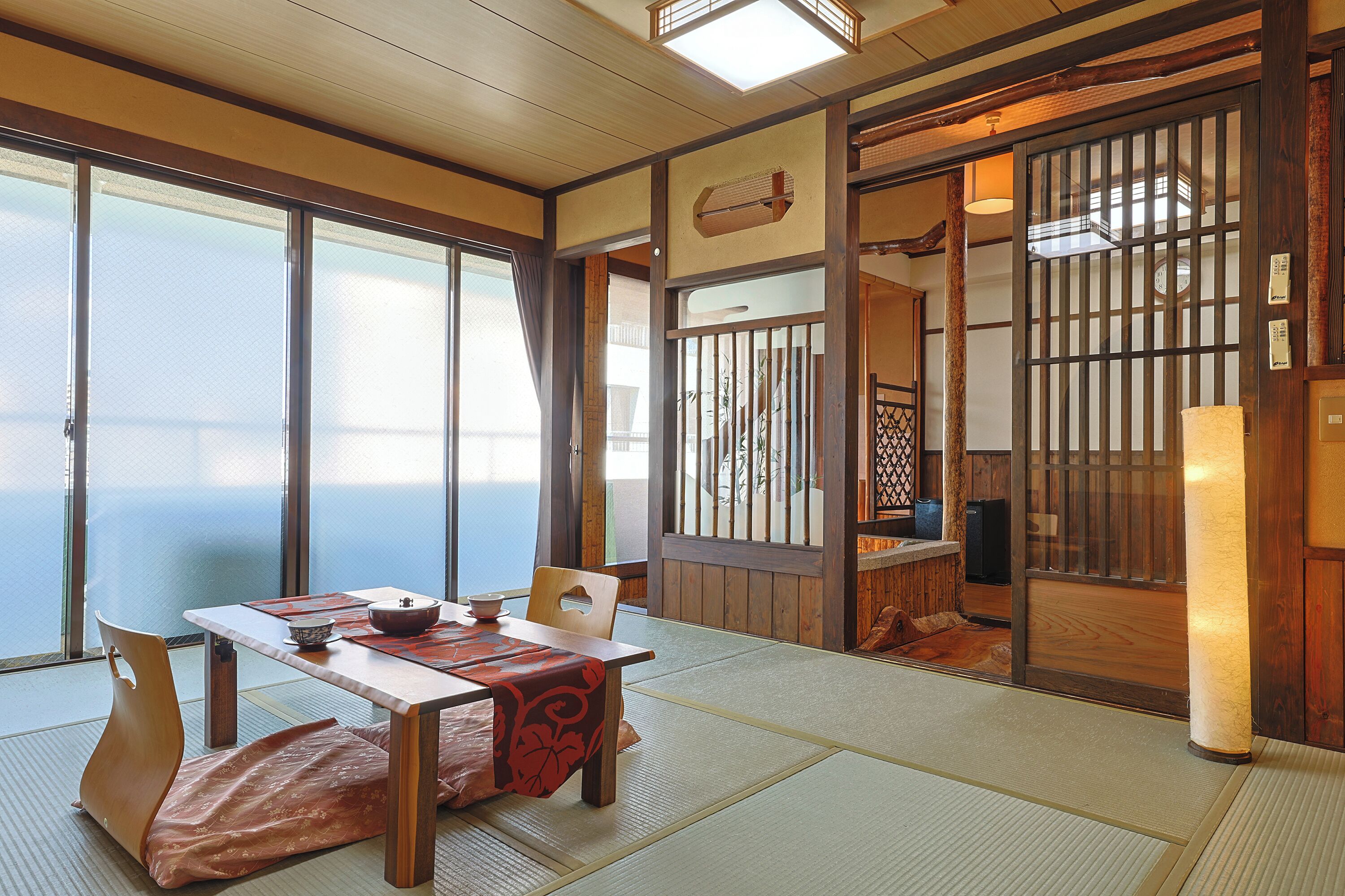 A traditional Japanese room with tatami flooring, a low table with a tea set, and sliding doors leading to another space.