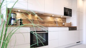 A modern kitchen with white cabinets, a built-in oven, a coffee maker, and a wooden backsplash. - Tradition meets modernity: captain's house on the Friedrichschleuse **** (Carolinensiel-Harlesiel)