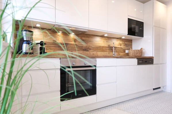 A modern kitchen with white cabinets, a built-in oven, a coffee maker, and a wooden backsplash.