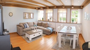 A living room with a sofa, coffee table, and dining table. There are windows with curtains, a clock on the wall, and a radiator. - Tradition meets modernity: captain's house on the Friedrichschleuse **** (Carolinensiel-Harlesiel)