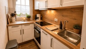 A kitchen with white cabinets, a wooden countertop, a coffee maker, a sink, and a trash bin.