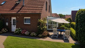 A brick house with a white door, a patio with a table and chairs, and a garden with flowers.