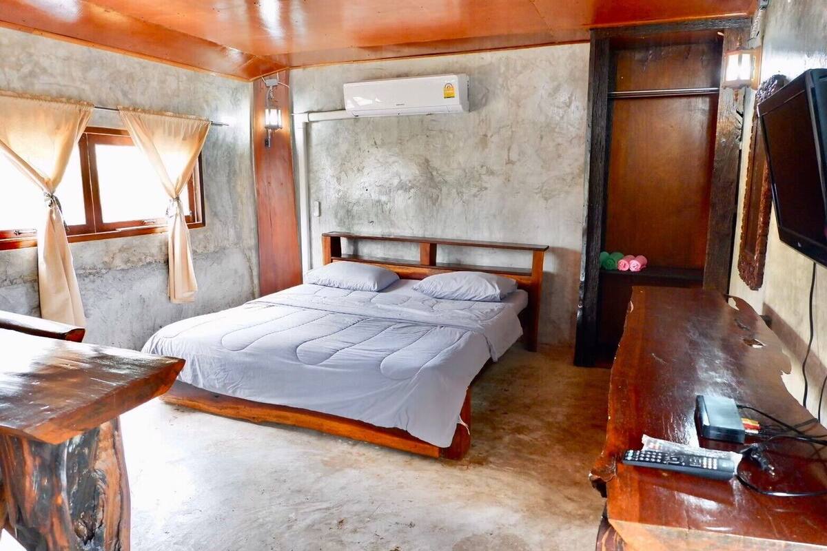 Una habitación con una cama, un escritorio de madera, un televisor y un equipo de aire acondicionado.