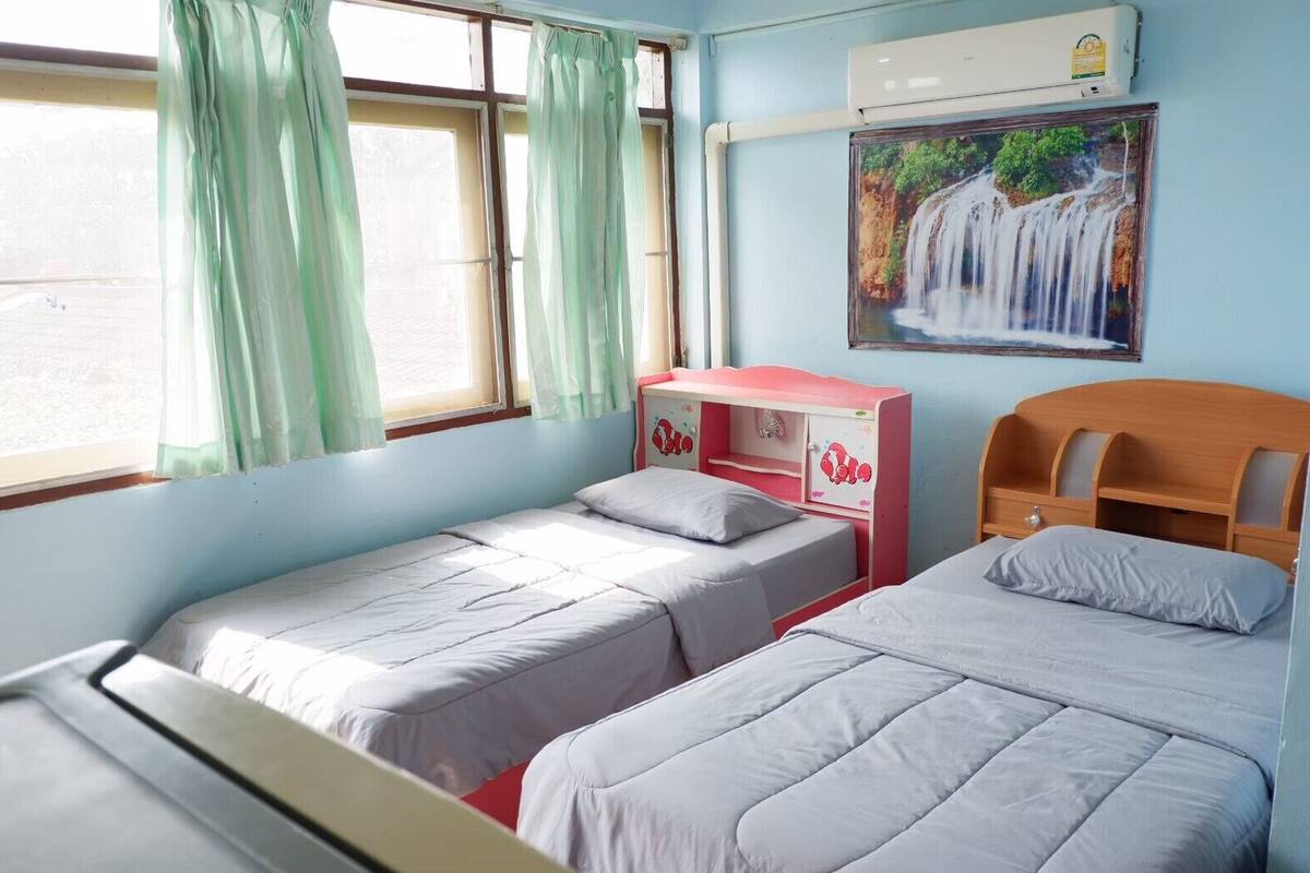 Una habitación con dos camas individuales, un aparador rosa, aire acondicionado instalado en la pared y un cuadro de una cascada.