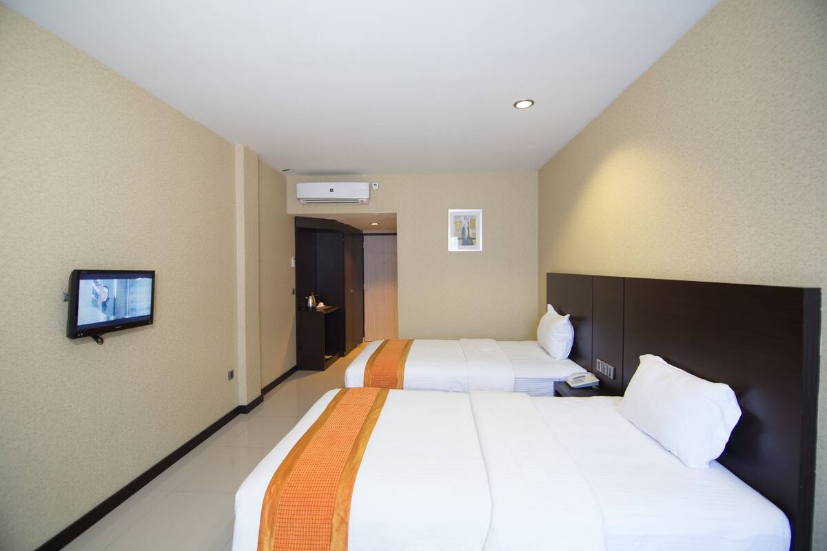 A hotel room with two beds, a television, an air conditioning unit, and a door leading to another room.