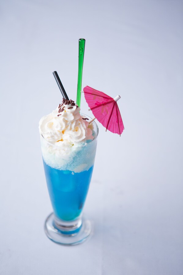 A tall glass with a blue liquid, topped with whipped cream and a pink umbrella.