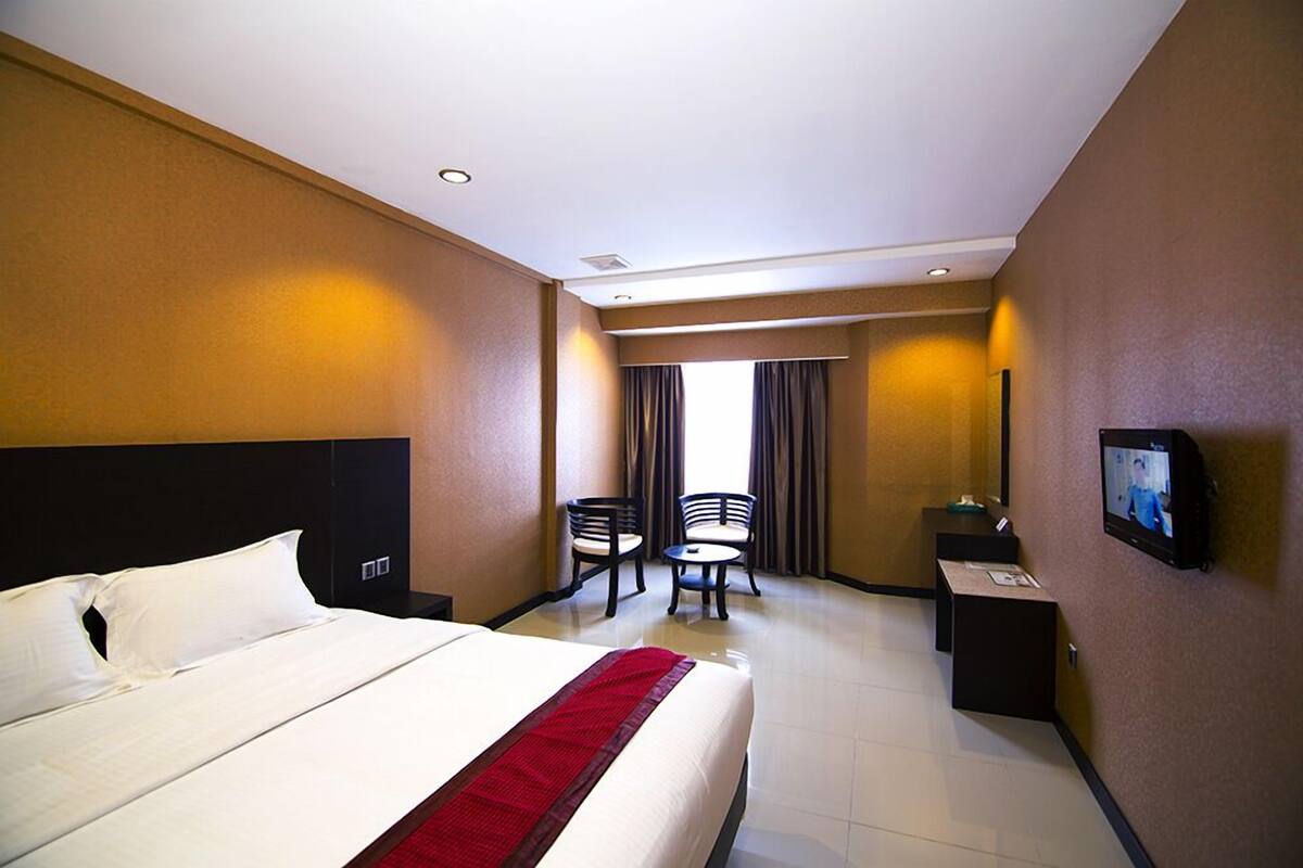 A hotel room with a large bed, a desk, two chairs, and a television on the wall.