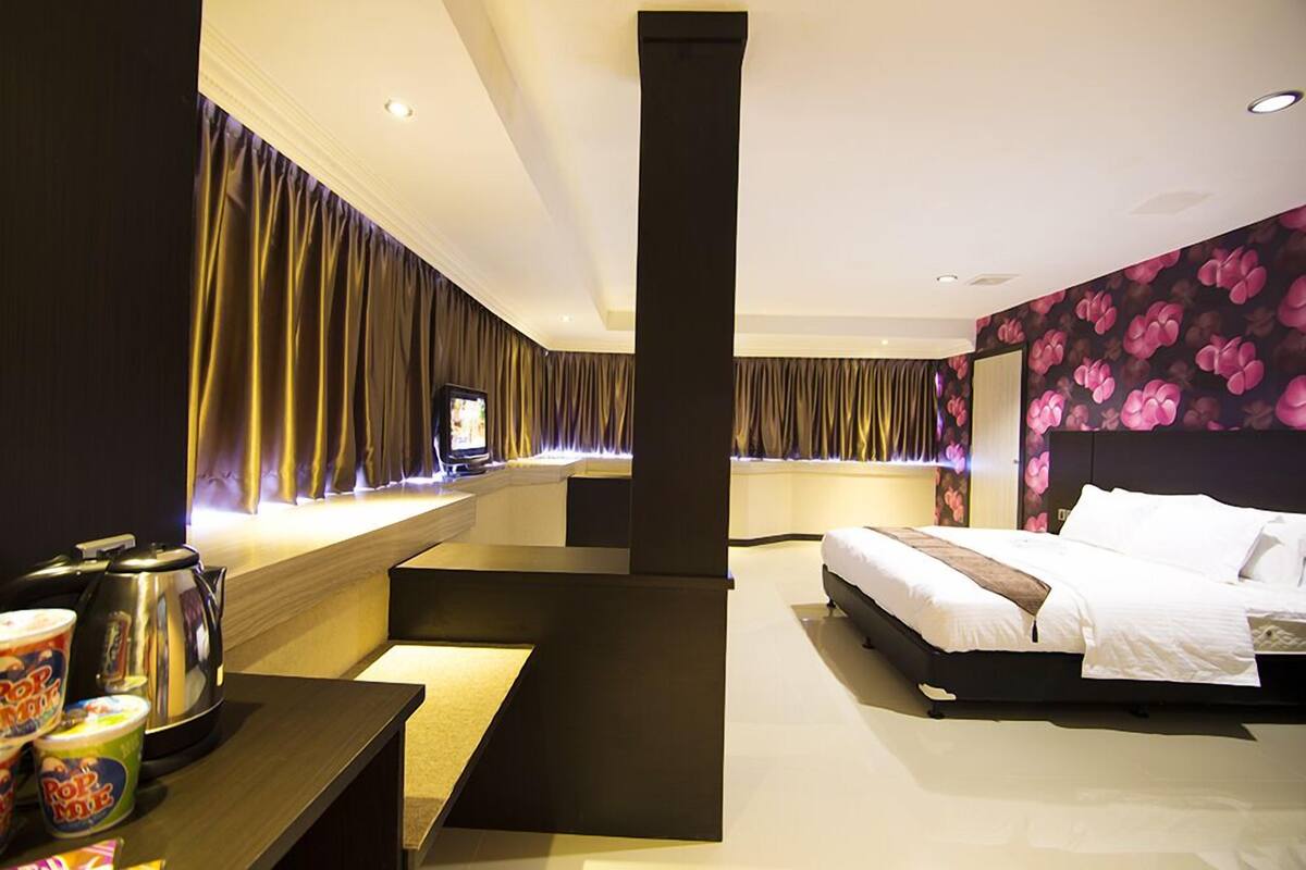 A modern hotel room with a large bed, a desk with a computer, and a minibar.