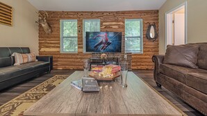 A living room with a wooden wall, a leather sofa, a coffee table with books and popcorn, and a TV displaying a Spider-Man movie.