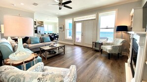 A spacious living room with a fireplace, a ceiling fan, and a view of the ocean through large windows. - Gulf front, North Cape, huge outdoor lounge, fenced pet area!!!! (Port St Joe)