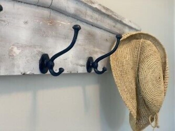 A wall-mounted wooden shelf with three black hooks and a woven basket.
