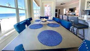 A dining area with a large table, blue chairs, and a view of the beach. - Gulf front, North Cape, huge outdoor lounge, fenced pet area!!!! (Port St Joe)