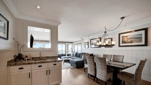 Een moderne keuken met witte kastjes, een eethoek met rieten stoelen en een groot raam dat natuurlijk licht binnenlaat.