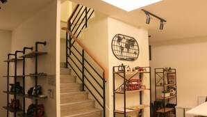 Una escalera con barandilla de madera y pasamanos negros, rodeada de estantes con diversos objetos.