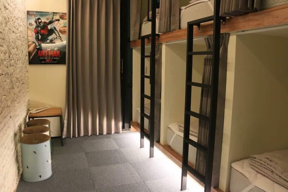 Habitación con literas, un cartel en la pared, una mesita y una cortina.