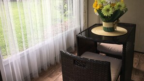 A wicker chair with a cushion, a small round table with a woven placemat, and a vase with flowers.
