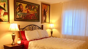 A bedroom with a bed, two bedside tables with lamps, a red throw pillow, a cowhide rug, and two paintings on the wall.