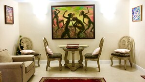 A living room with a beige sofa, two armchairs, a round table, and a large painting on the wall.