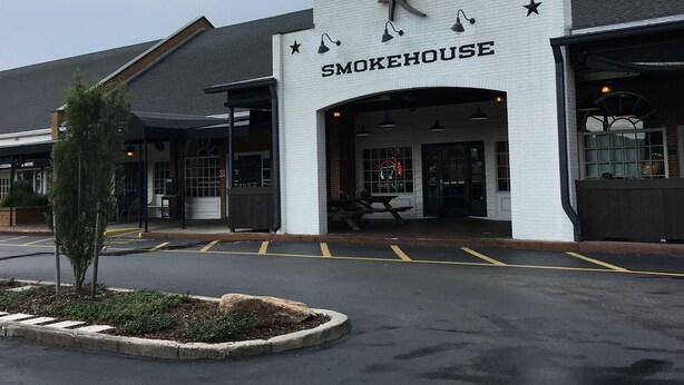 A Smokehouse restaurant with a white facade, a black awning, and a parking lot in front.