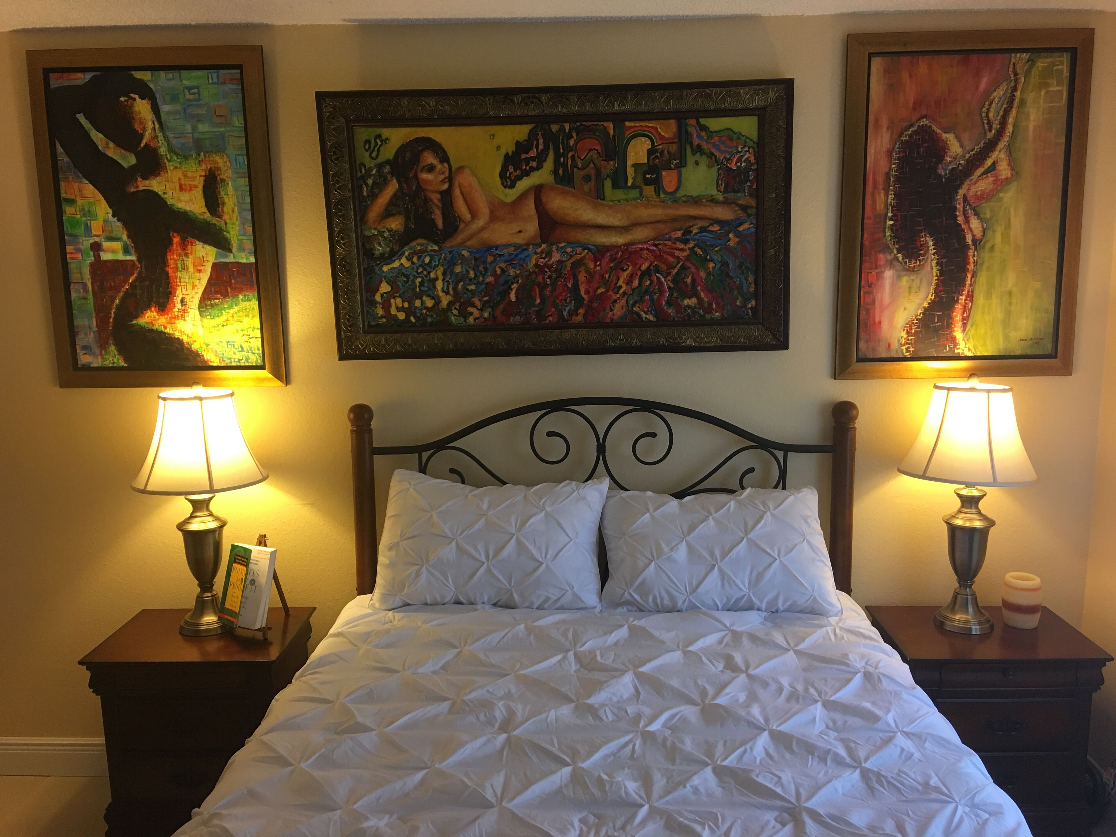A hotel room with a bed, two nightstands, two lamps, and three paintings on the wall.
