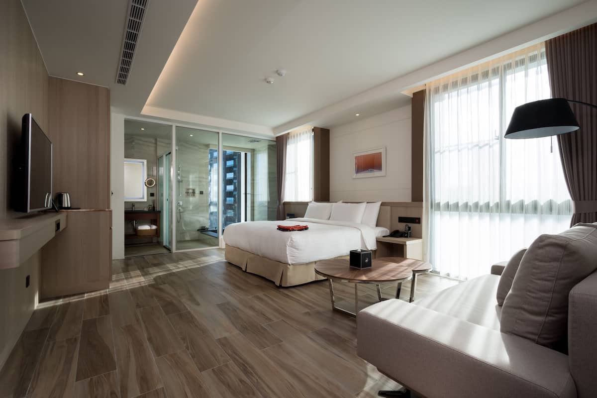 Une chambre d’hôtel moderne dotée d’un grand lit, d’un canapé, d’une télévision et d’une porte vitrée donnant sur un balcon.