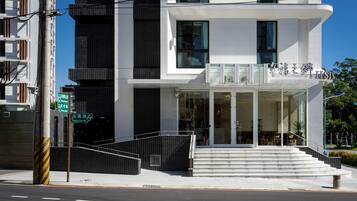 A modern building with a white facade, large windows, and a visible entrance with steps leading up to it.