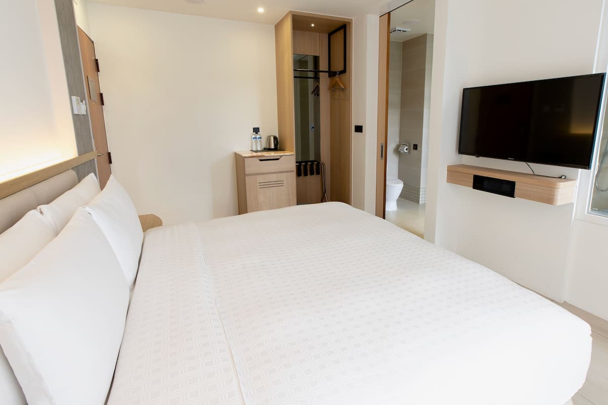 Une chambre d’hôtel avec un grand lit, un téléviseur fixé au mur, une petite table de chevet et un dressing.