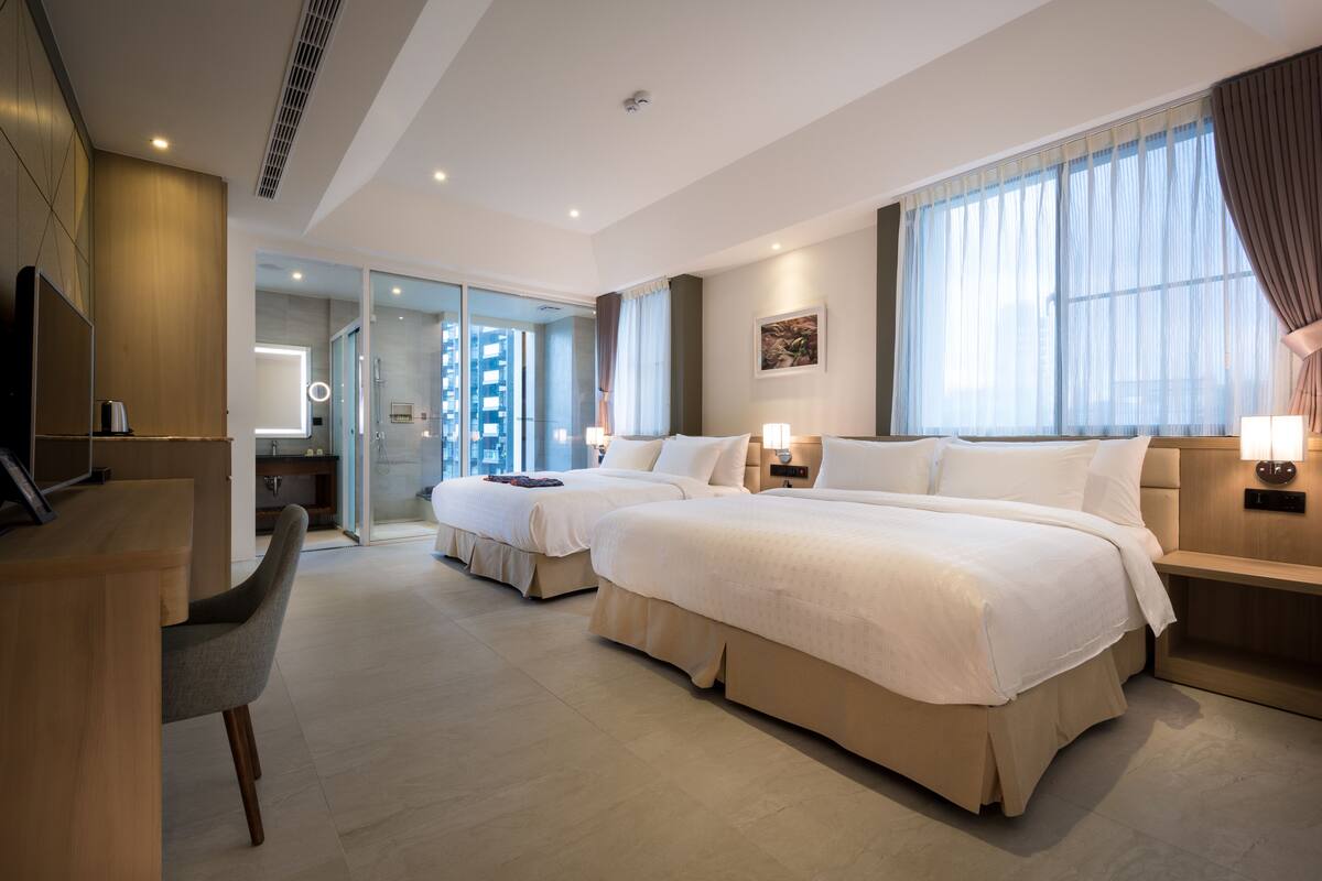 Une chambre d’hôtel moderne avec un grand lit, un bureau et une chaise. On peut apercevoir la salle de bain à travers une porte ouverte.