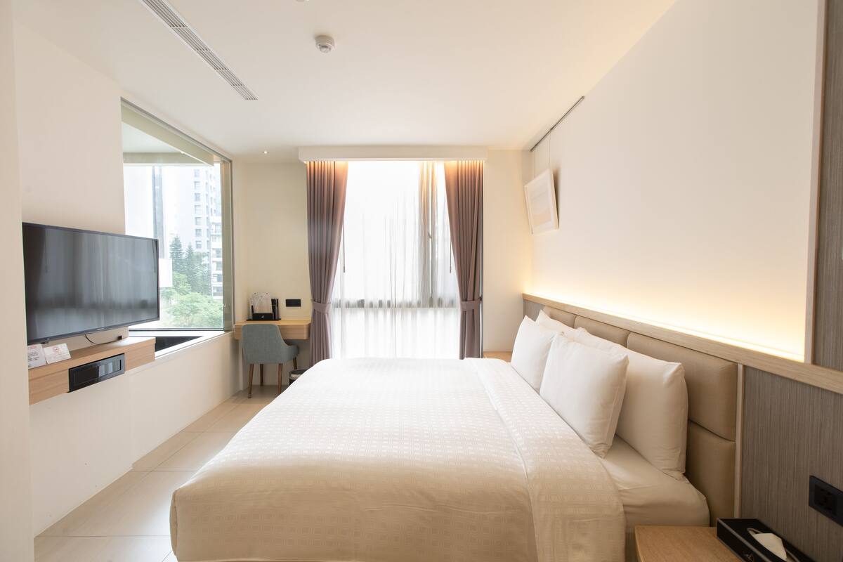 Une chambre d’hôtel avec un grand lit, une télévision, un bureau et une fenêtre avec des rideaux.