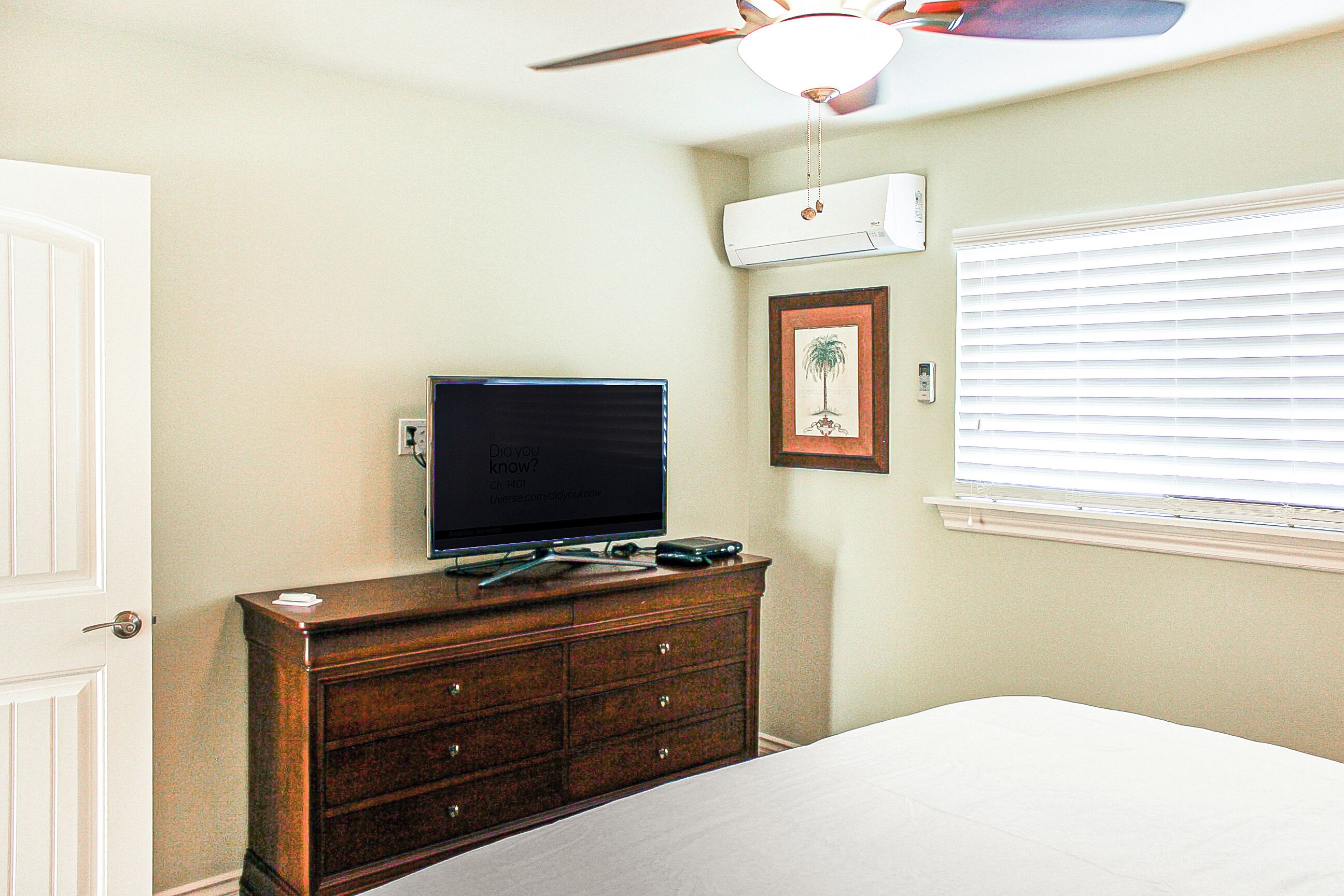 A bedroom with a bed, a dresser, a television, an air conditioning unit, and a ceiling fan.